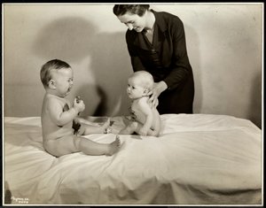 Dos bebés sentados en la cama, uno sostenido por una enfermera, el otro con un coche de juguete y llorando en el Centro de Maternidad en la calle 70 East River, Nueva York, 1935